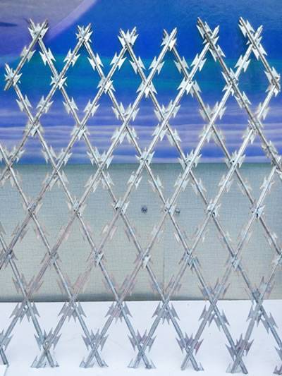 Galvanized welded razor wire mesh with diamond mesh holes is against the wall.
