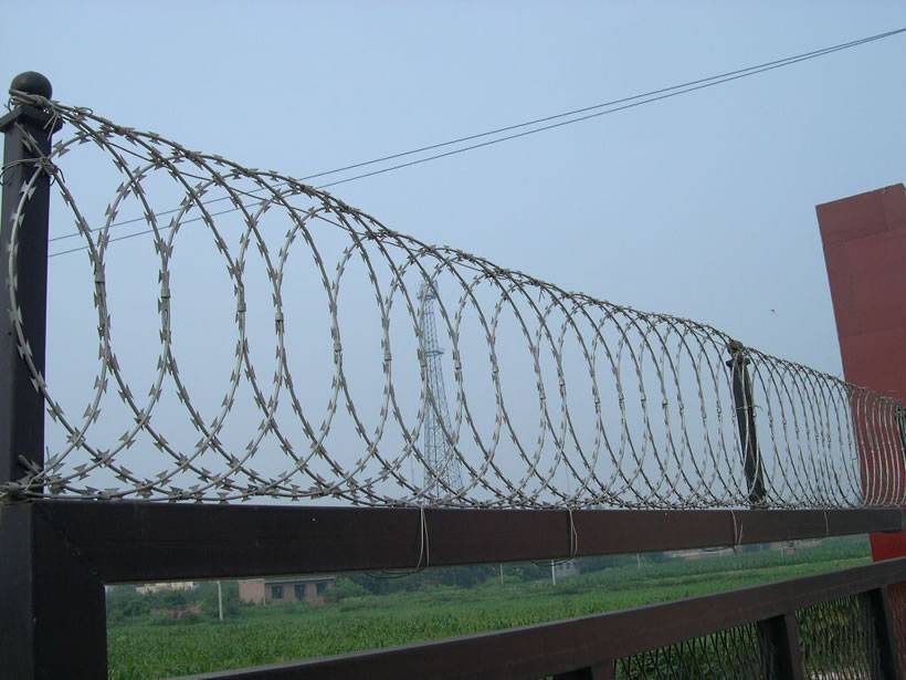 A row of flat wrap razor wire is installed on metal bar as security fence.