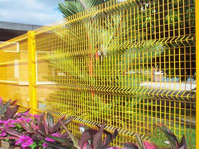 A yellow PVC coated welded wire 3D security fence with four curves is installed at a garden.