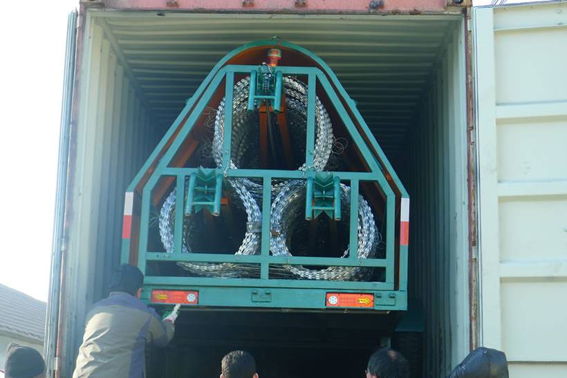 A green razor wire trailer deployment is installed into a red color container on a big truck.