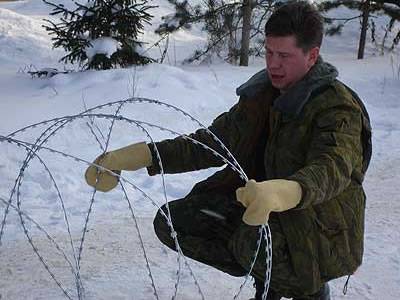 A man is stretching a spiral concertina razor wire coil on the snow ground