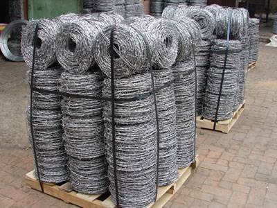 Many coils of barbed wire is packed with bailing strip on wooden pallet.