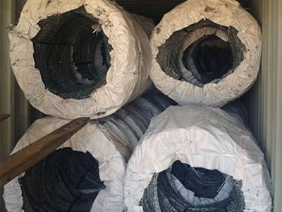 Many coils of concertina barbed wire are packed with white PP woven bag in container.