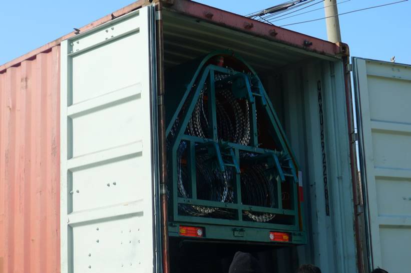 A green razor wire trailer with triple strand of razor wire has been in a red color container.