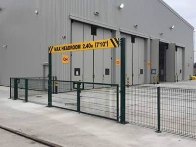 A green roll top fence with a gate is installed at a large factory site.