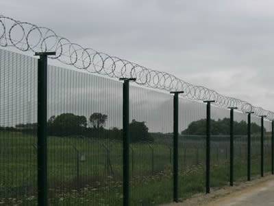 With razor wire topping, a dark green PVC coated prison security fence is installed between farm and road.