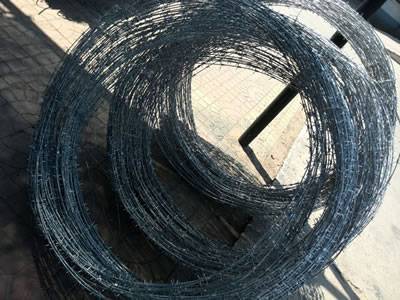 Three coils of concertina barbed wire are against a post.