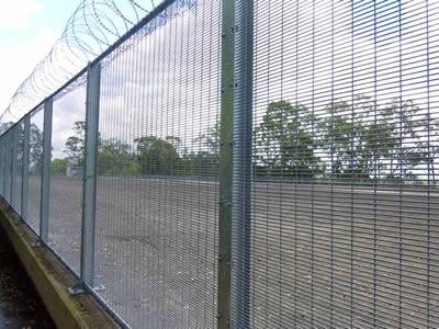 With razor wire topping, a galvanized prison security fencing is installed between the road and a piece of land.