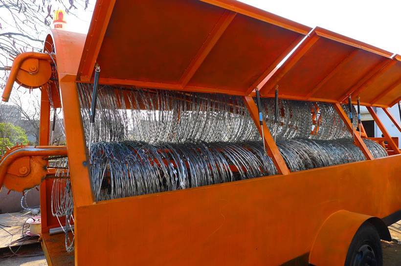 Three coils of galvanized razor wire is in orange color trailer and the side gate of trailer is opening.