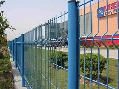 A blue 2-curve welded wire 3D security fence with peach posts is installed behind a office building.
