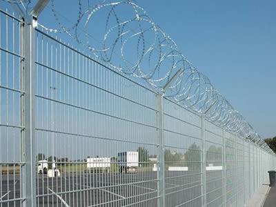 A galvanized welded wire fence combining with razor wire separates an airport at which cars stop from the outside world.
