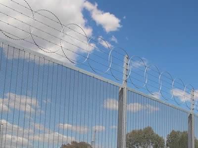 A welded wire mesh combining barbed razor wire separates a industrial machines site from outside world.